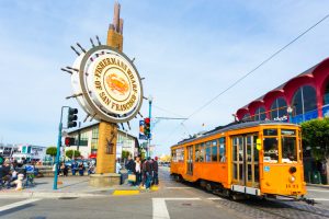 San Francisco, United States - May 5, 2016: Orange vintage Swiss F Market streetcar rolls by large sign at entrance to the tourist attraction of Fisherman's Wharf on the corner of Beach and Jones Street. Horizontal